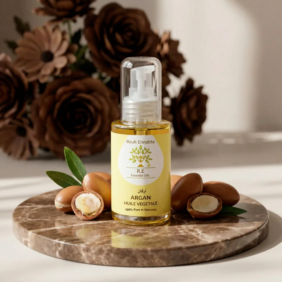 Bottle of Huile d'Argan Pure BIO – Trésor Anti-âge with argan nuts on a marble surface and decorative brown flowers in background