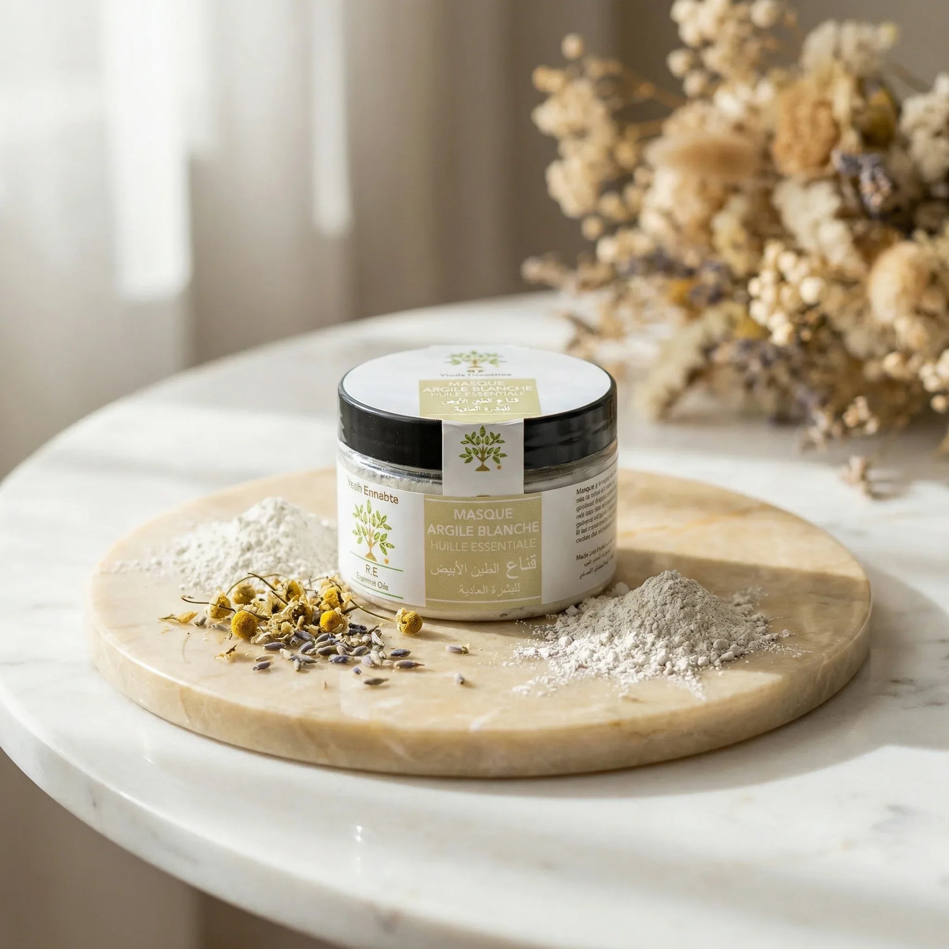 Masque Douceur à l'Argile Blanche jar with natural white clay and dried flowers on marble surface in soft light
