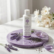 Nettoyant Visage Doux à la Lavande face wash bottle on purple marble with lavender sprigs and white flowers in soft light