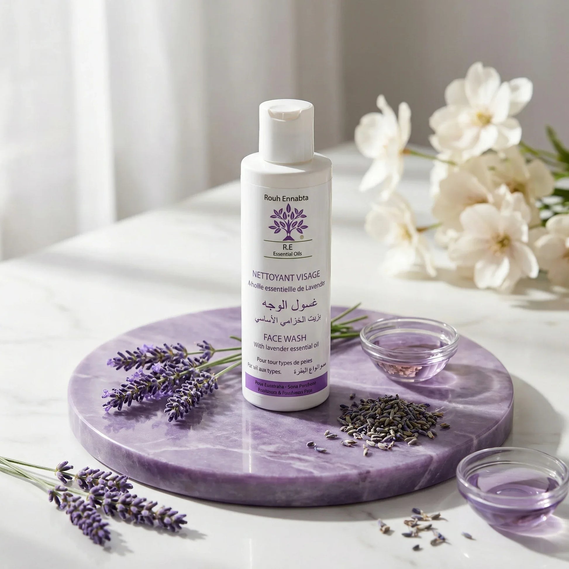 Nettoyant Visage Doux à la Lavande face wash bottle on purple marble with lavender sprigs and white flowers in soft light