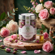 Glass jar of dried Damascena rose petals surrounded by fresh pink roses and a small bottle of rose essential oil, Pétales de Rose de Damas BIO – Bain Luxe.