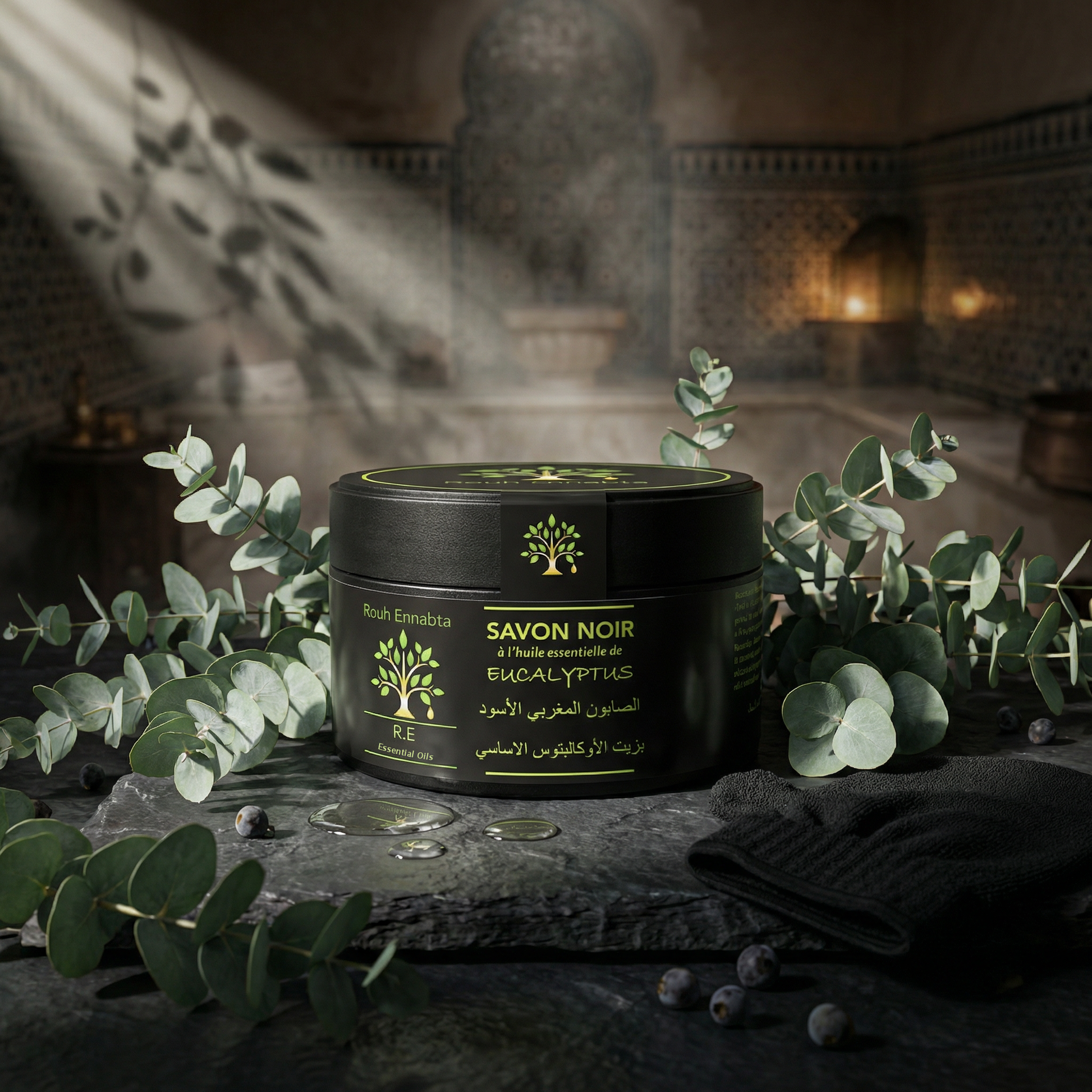 Black jar of Savon Noir Artisanal à l'Eucalyptus | Peau douce, lisse & purifiée with eucalyptus leaves on stone surface