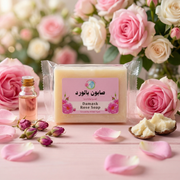 Savon à la Rose de Damas – Douceur Quotidienne Tous Types de Peau with rose petals, oil, and cream on a pink surface.