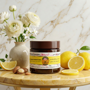 Savon Noir à l'Argan et Citron· Peau Purifiée, Hydratée & Teint Éclatant jar with argan nuts and lemons on a marble table with white flowers.